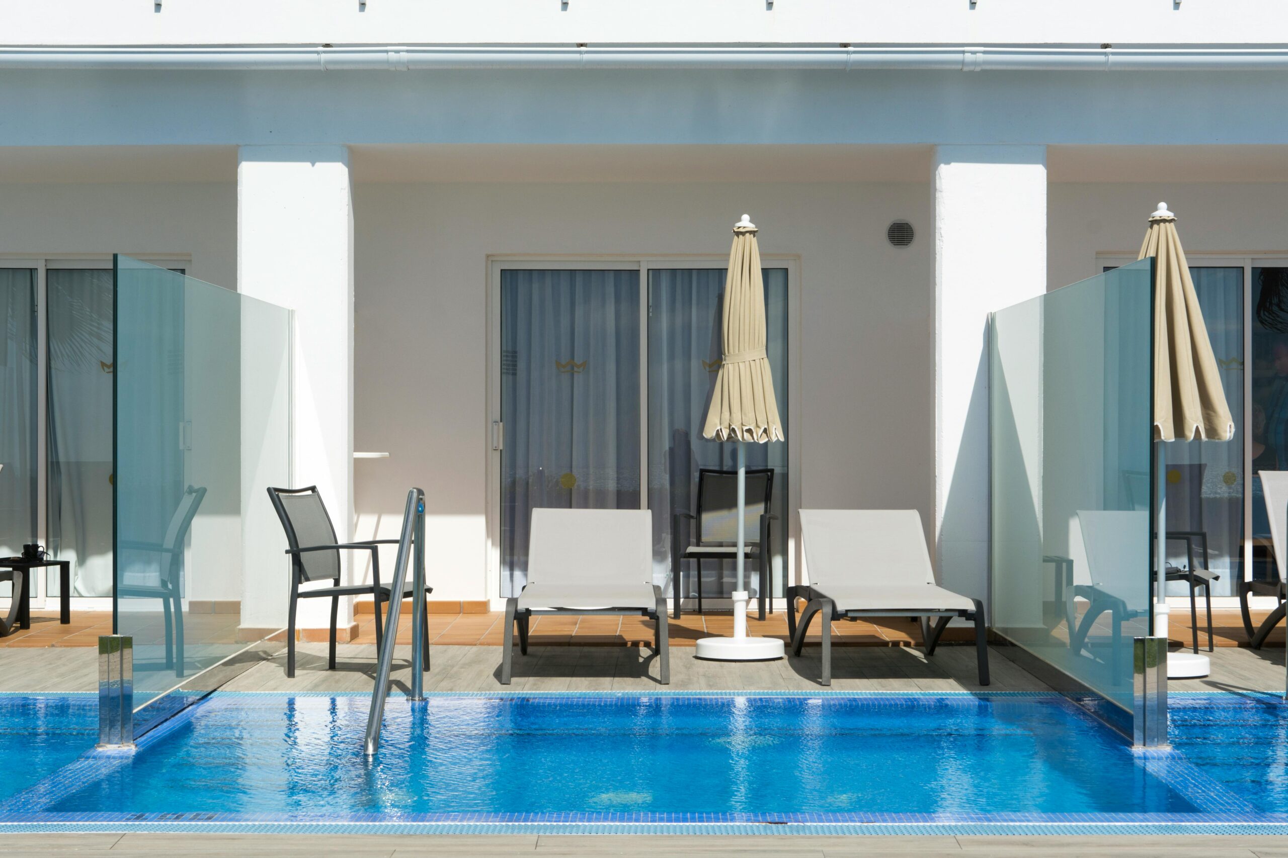 Modern luxury villa poolside scene with sun loungers and umbrellas, perfect for relaxation.